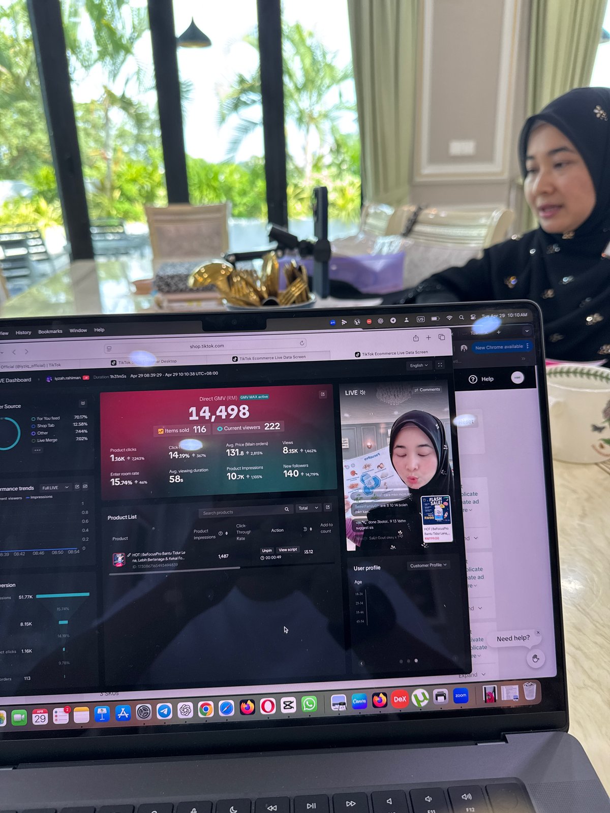 Komputer riba memaparkan sesi live, dengan wanita yang sedang bersiaran di belakangnya