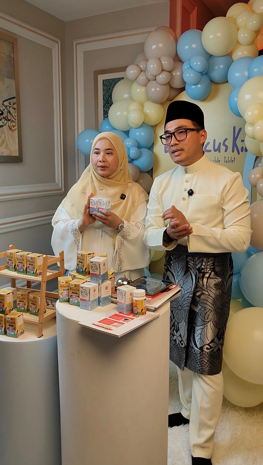 Najib dan seorang wanita memperkenalkan produk dengan hiasan belon pastel di belakang mereka